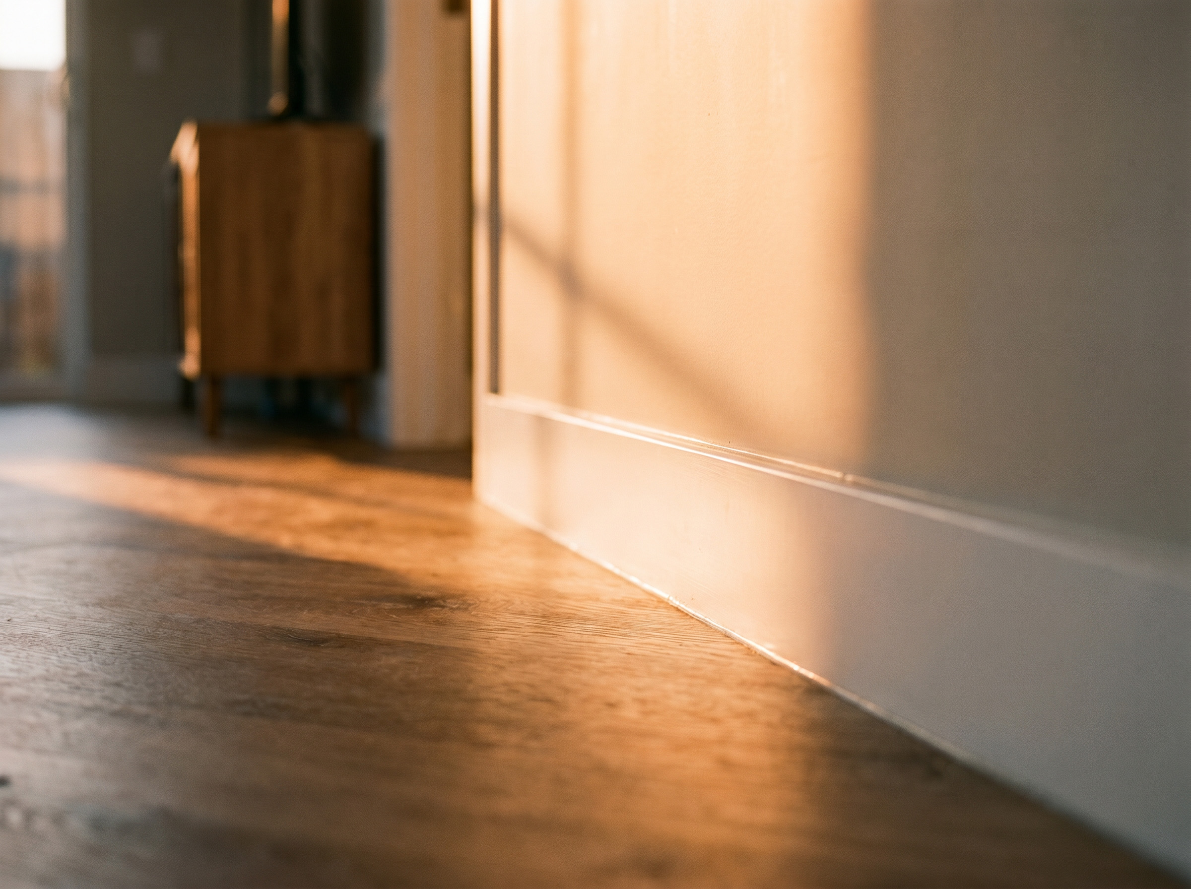 Close-up van een strak afgewerkte plint langs een houten vloer, verlicht door warm invallend zonlicht.